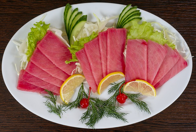 Raw slices of fish on platter with vegetables and lime