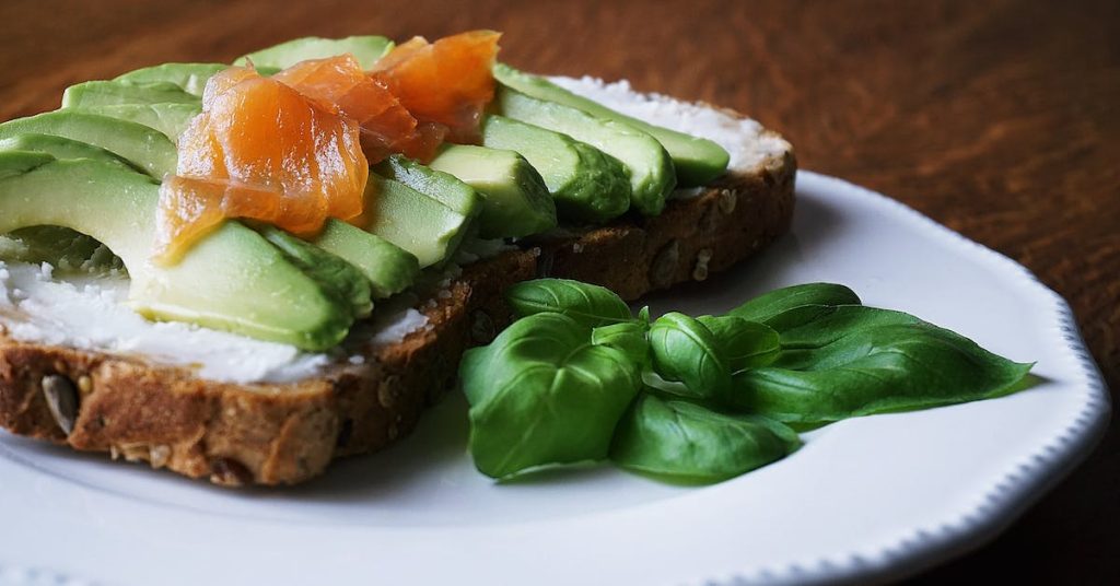 bread-with-sliced-avocado-and-salmon-near-basil-mint-on-plate