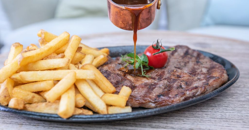 pouring sauce on steak-and-french-fries-on-black-plate